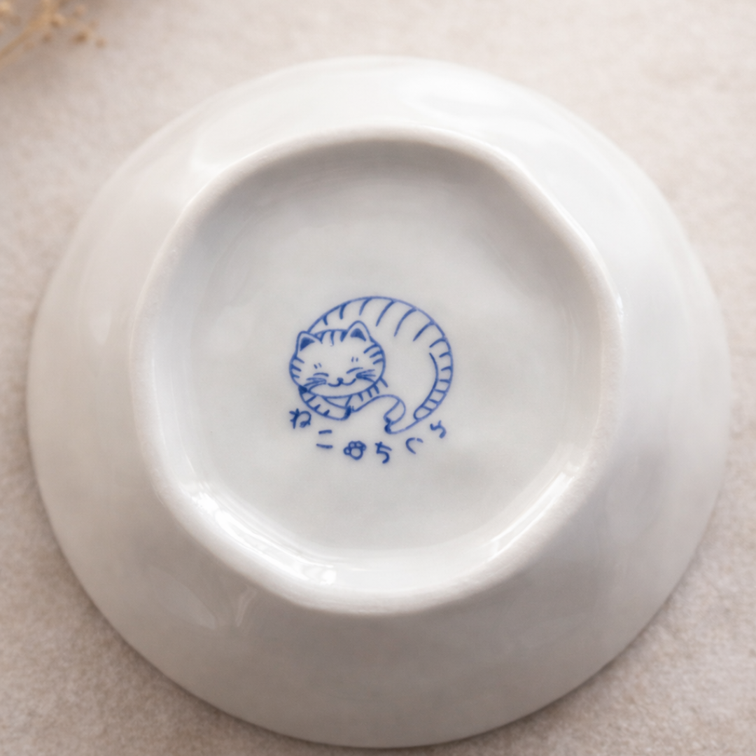 White ceramic plate with blue cat illustration on a beige surface