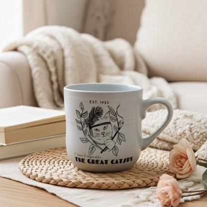White mug with black cat illustration and text on a woven coaster with flowers and books in the background