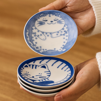Hand holding a stack of small ceramic plates with cat designs on a wooden surface