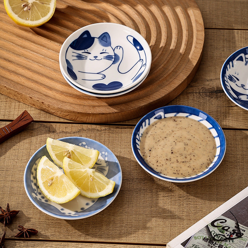 Set of small ceramic dishes with blue cat design on a wooden surface with lemon slices and a bowl of sauce.