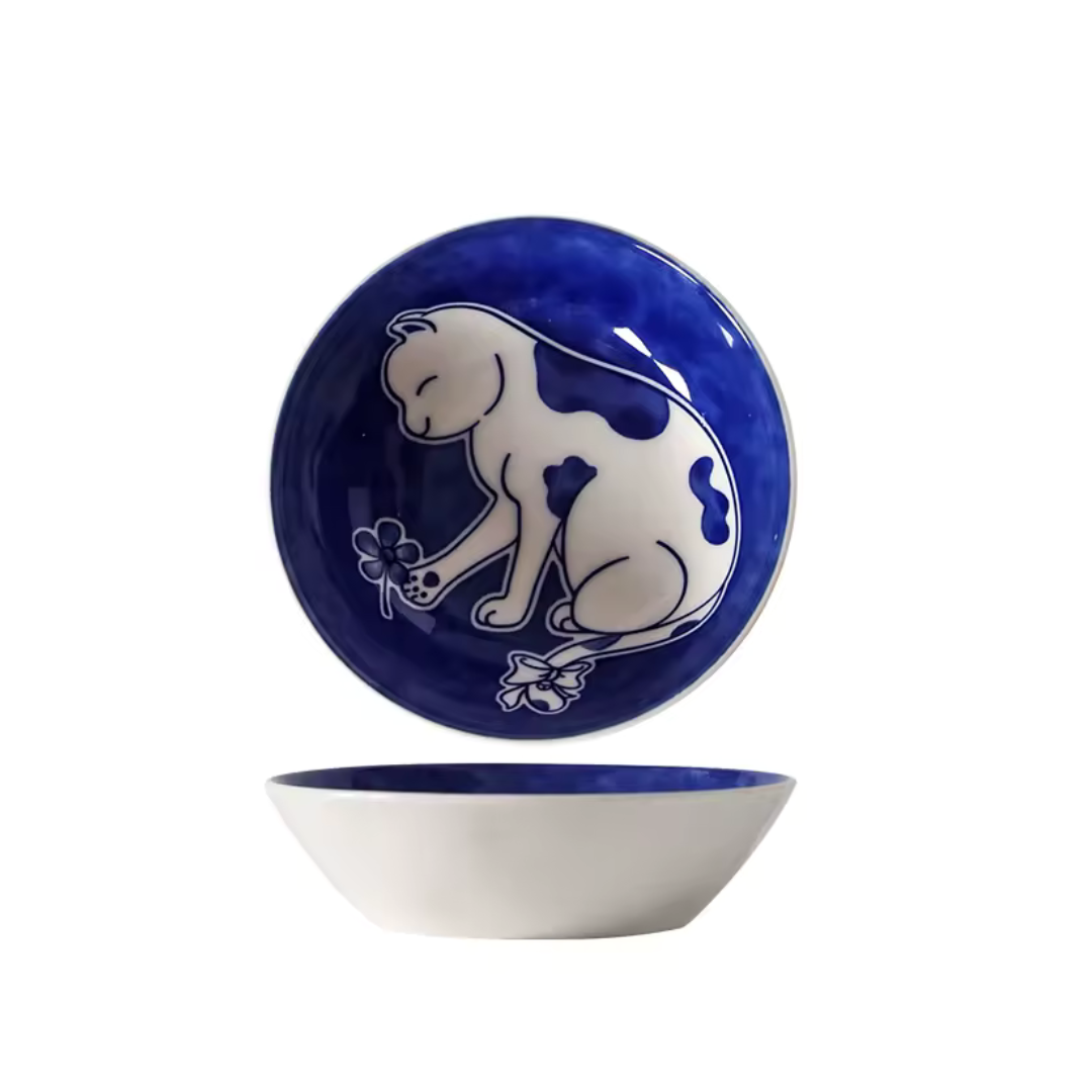 Ceramic bowl with blue rim and white cat design on a white background