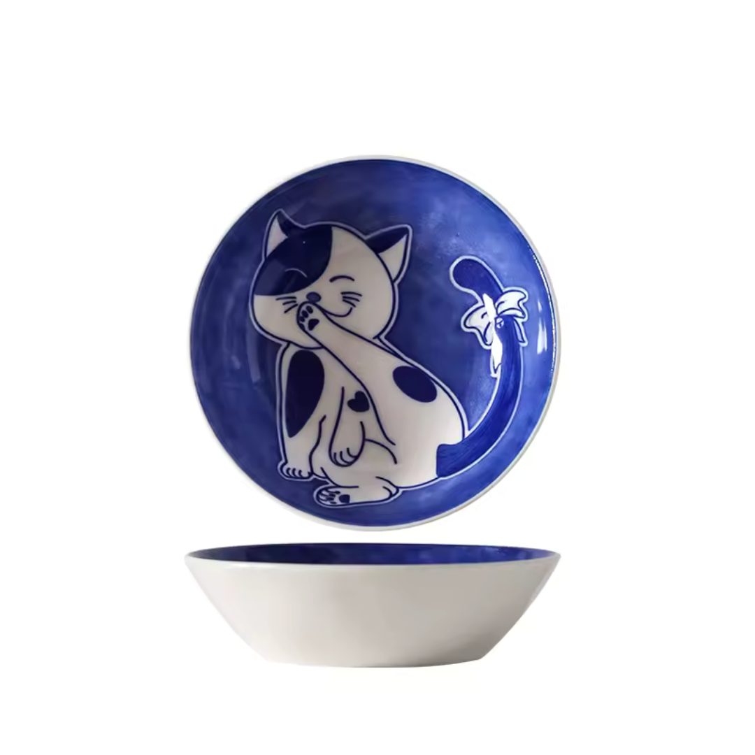 Ceramic bowl with blue interior and white exterior featuring a smiley shy cat design on a white background